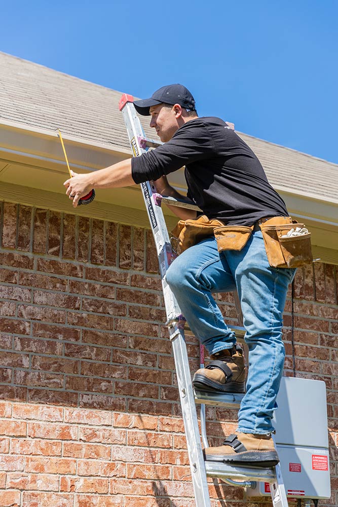 Roofer on ladder inspecting roof of house